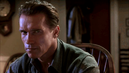 A Man Is Sitting In A Chair With A Clock Behind Him GIF