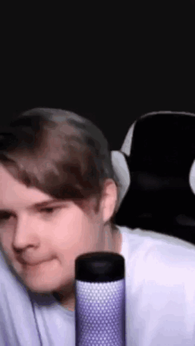 A Man Is Sitting In A Chair With A Microphone In Front Of Him And Smiling . GIF