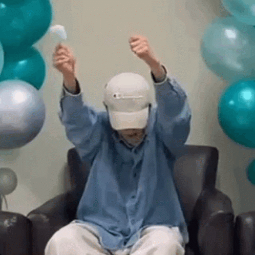 A Man Is Sitting In A Chair With His Arms In The Air And Holding A Balloon . GIF