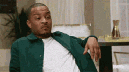 A Man Is Sitting In A Chair With His Hand On His Shoulder . GIF
