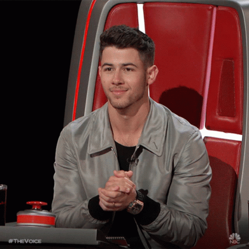 A Man Is Sitting In A Chair With His Hands Folded In Front Of A Nbc Button GIF