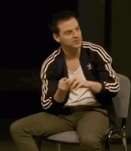 A Man Is Sitting In A Chair With His Hands On His Chest . GIF