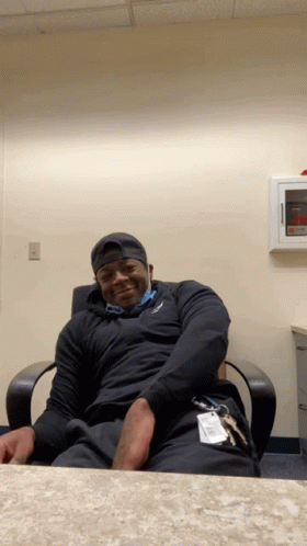 A Man Is Sitting In A Chair With His Hands On His Hips And A Name Tag That Says ' Johnson ' On It GIF
