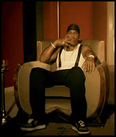 A Man Is Sitting In A Chair With His Legs Crossed And Smoking A Cigarette . GIF