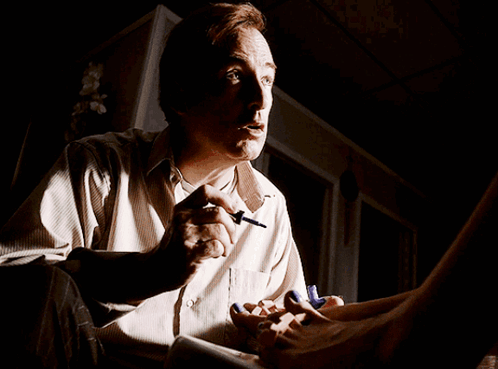 A Man Is Sitting In A Dark Room With A Woman 'S Feet On His Lap GIF