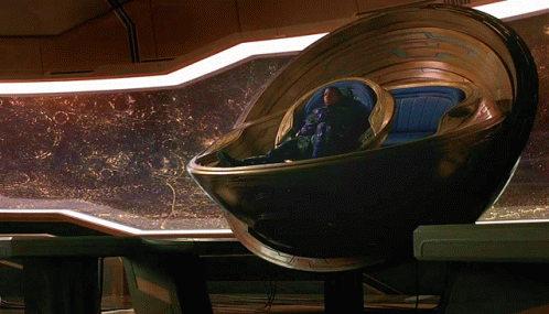 A Man Is Sitting In A Futuristic Chair With A Blue Seat GIF