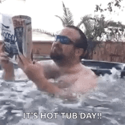 a man is sitting in a hot tub reading a book while holding a can of beer .