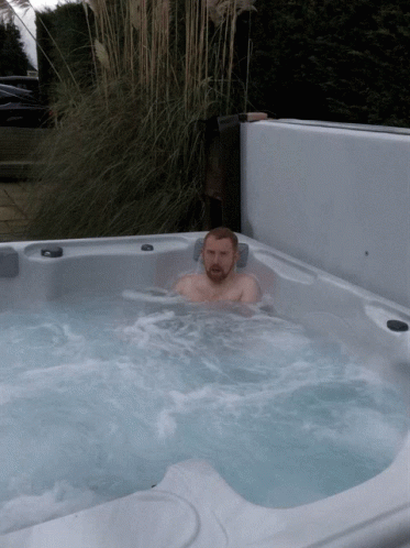 a man is sitting in a hot tub with a plant in the background