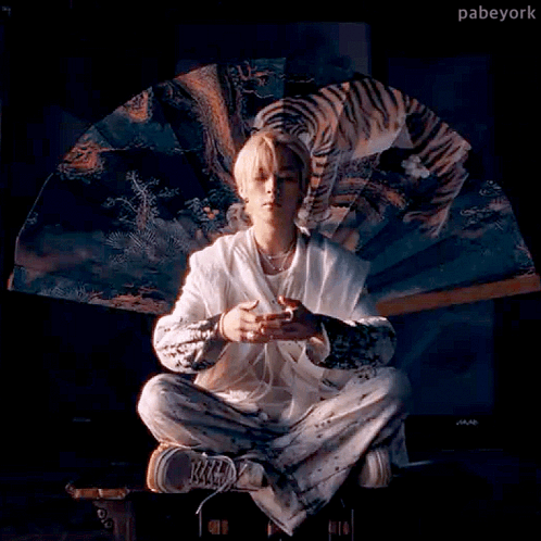 A Man Is Sitting In A Lotus Position Holding A Fan With A Picture Of A Tiger On It . GIF