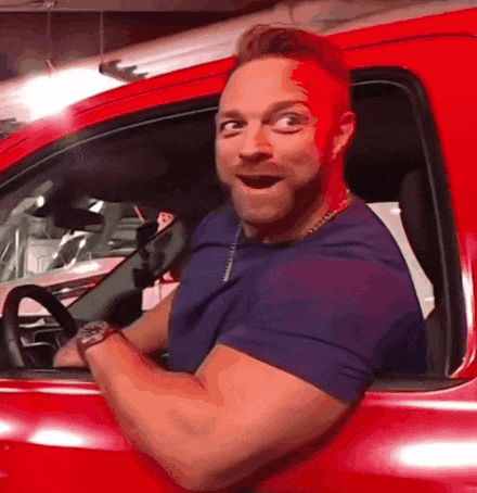 A Man Is Sitting In A Red Car With His Mouth Open GIF