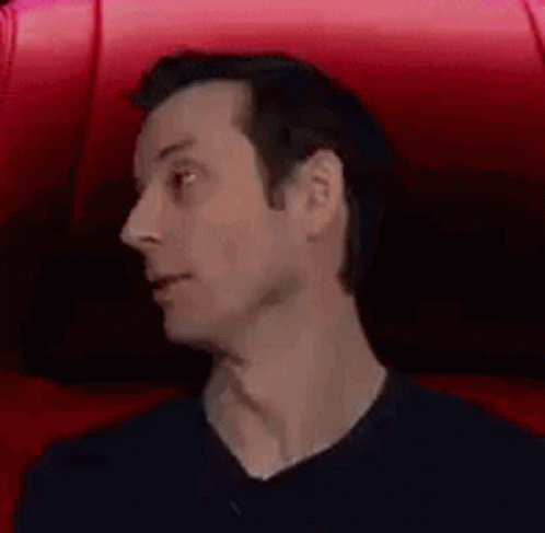 A Man Is Sitting In A Red Chair With His Mouth Open And A Surprised Look On His Face . GIF