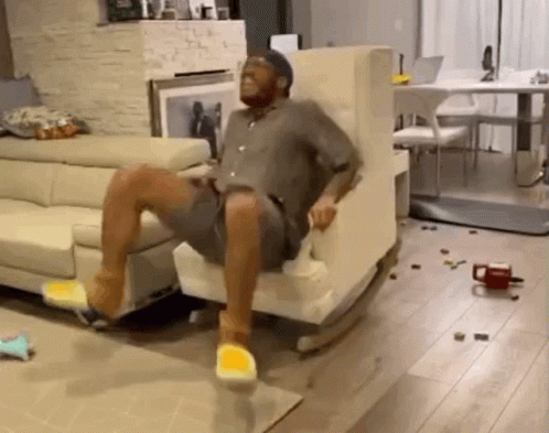 A Man Is Sitting In A Rocking Chair In A Living Room With A Couch . GIF