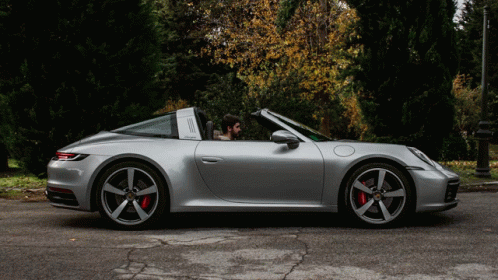 A Man Is Sitting In A Silver Porsche Targa GIF