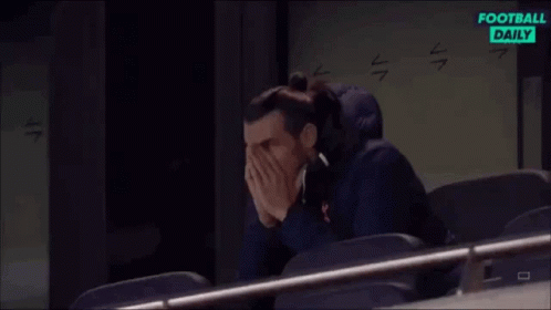 A Man Is Sitting In A Stadium Covering His Face With His Hands While Watching A Football Game . GIF