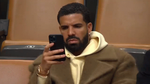 A Man Is Sitting In A Stadium Looking At His Phone . GIF