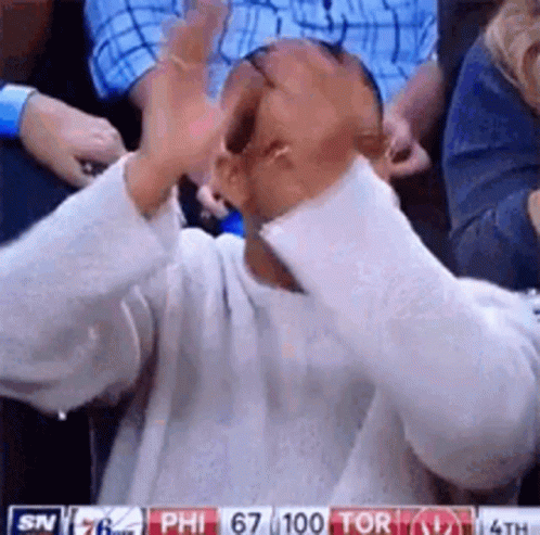A Man Is Sitting In A Stadium Watching A Basketball Game And Covering His Face With His Hands . GIF