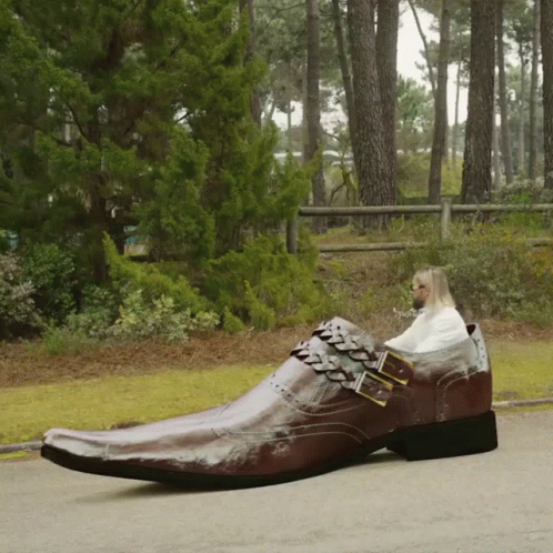 A Man Is Sitting In A Very Large Brown Shoe GIF