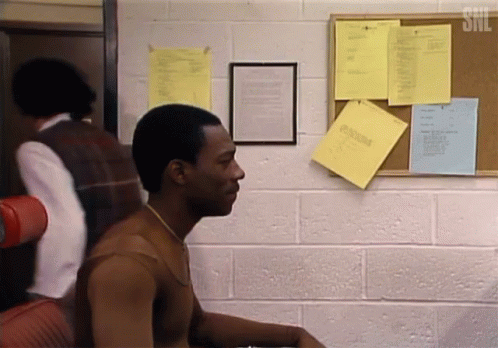 A Man Is Sitting In Front Of A Bulletin Board With A Snl Logo On It GIF