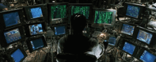 A Man Is Sitting In Front Of A Bunch Of Computer Monitors With The Word Matrix On The Screens GIF