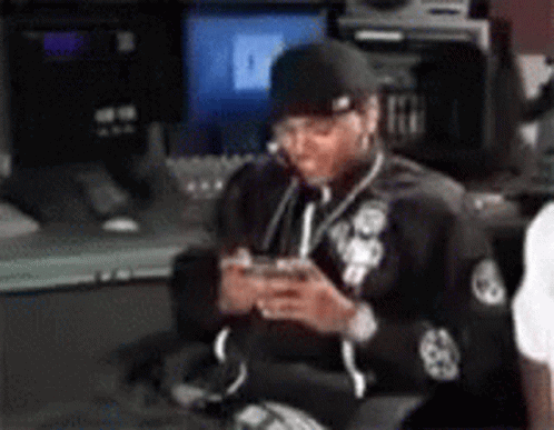 A Man Is Sitting In Front Of A Computer And Looking At His Phone . GIF