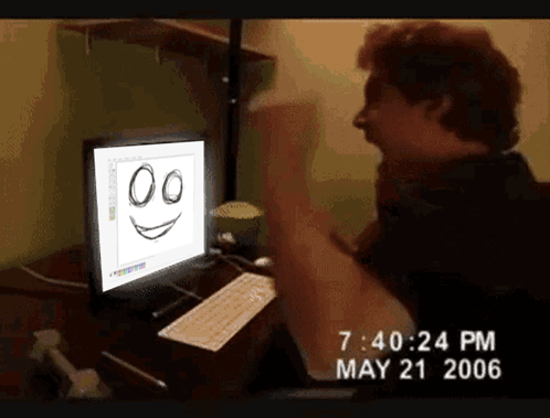 A Man Is Sitting In Front Of A Computer With A Smiley Face On It GIF