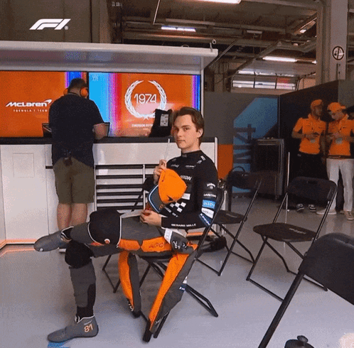 A Man Is Sitting In Front Of A Mclaren Sign GIF