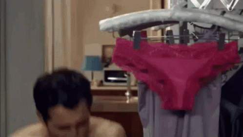 A Man Is Sitting In Front Of A Rack Of Pink Underwear . GIF