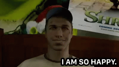 A Man Is Sitting In Front Of A Shrek Poster And Says " I Am So Happy " GIF
