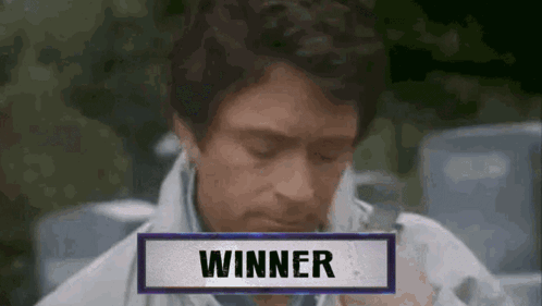 A Man Is Sitting In Front Of A Sign That Says " Winner " GIF