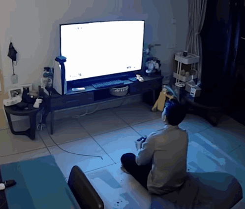 A Man Is Sitting In Front Of A Television With A White Screen GIF