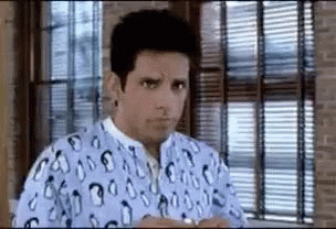 A Man Is Sitting In Front Of A Window Wearing A Hospital Gown . GIF