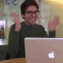 A Man Is Sitting In Front Of An Apple Laptop Computer . GIF
