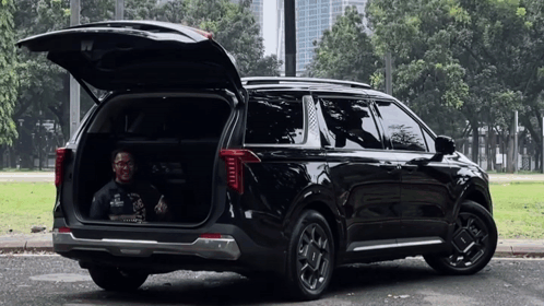 A Man Is Sitting In The Back Of A Black Suv With Its Trunk Open . GIF
