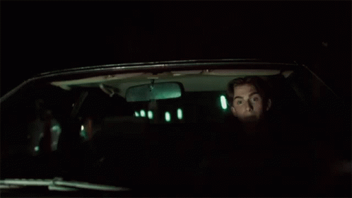 A Man Is Sitting In The Back Seat Of A Car At Night Looking Out The Window . GIF