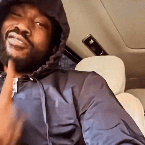 A Man Is Sitting In The Back Seat Of A Car Wearing A Hooded Jacket . GIF