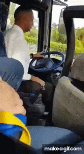 A Man Is Sitting In The Driver 'S Seat Of A Bus While A Child Sits In The Back Seat . GIF