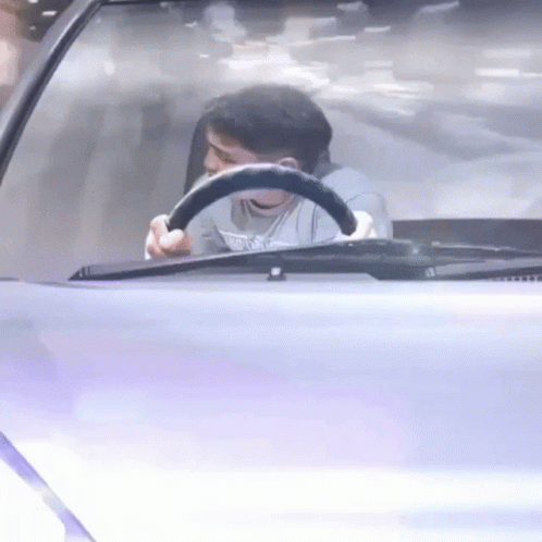 A Man Is Sitting In The Driver 'S Seat Of A Car Holding A Steering Wheel . GIF