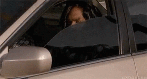 A Man Is Sitting In The Driver 'S Seat Of A Car Looking Out The Window . GIF