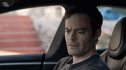 A Man Is Sitting In The Driver 'S Seat Of A Car Looking Out The Window . GIF