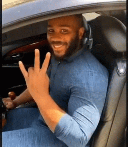 A Man Is Sitting In The Driver 'S Seat Of A Car Making A Peace Sign . GIF