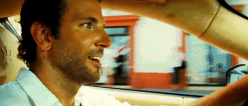 A Man Is Sitting In The Driver 'S Seat Of A Car While A Woman Holds His Hand Over His Head . GIF