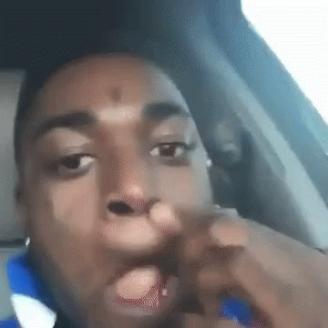 A Man Is Sitting In The Driver 'S Seat Of A Car With His Hand In His Mouth . GIF