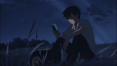 A Man Is Sitting In The Grass Looking At His Cell Phone GIF