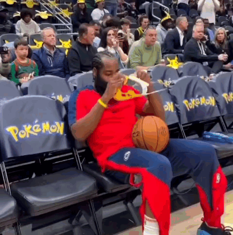 A Man Is Sitting In The Stands Holding A Basketball And Eating Pizza . GIF