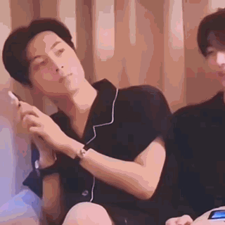 A Man Is Sitting On A Bed Smoking A Cigarette While Another Man Looks On . GIF
