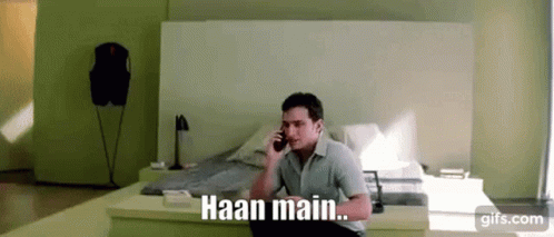A Man Is Sitting On A Bed Talking On A Cell Phone With The Words Haan Main . GIF