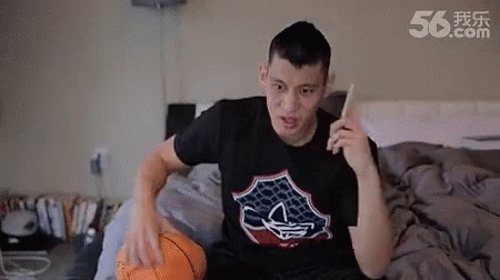 A Man Is Sitting On A Bed With A Basketball And A Cell Phone . GIF