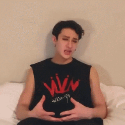 A Man Is Sitting On A Bed With His Hands On His Belly . GIF