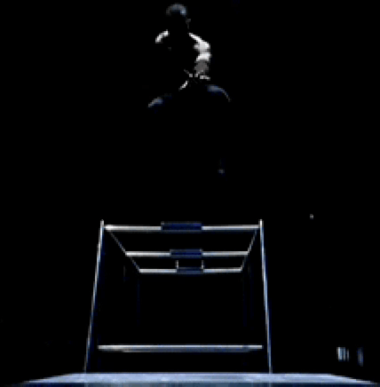 A Man Is Sitting On A Chair In The Dark With His Legs Crossed GIF