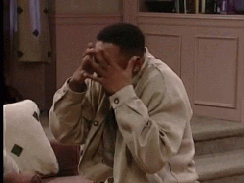 A Man Is Sitting On A Couch And Covering His Face With His Hands . GIF